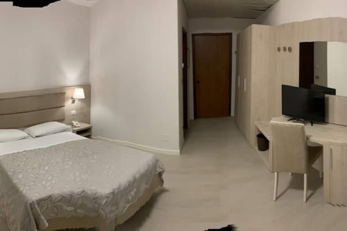 A hotel room with a bed, bedside table, lamp, desk, chair, and a TV.