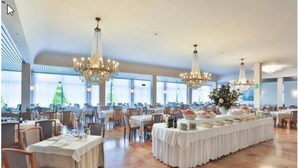 A spacious dining area with multiple tables, chandeliers, and large windows. - Hotel Smeraldo (Abano Terme)