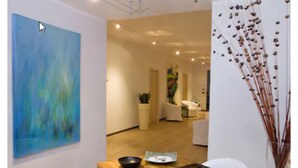 A modern interior with a large abstract painting, a wooden reception desk, and a decorative plant arrangement. - Hotel Smeraldo (Abano Terme)