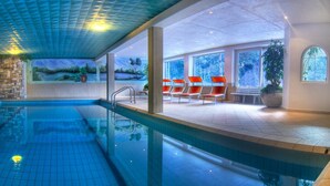 An indoor swimming pool with clear blue water, stone walls, and a mural depicting a landscape. - Sporthotel Spögler (Renon)
