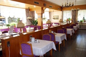 Un restaurante con paneles de madera, sillas tapizadas en morado y manteles blancos.