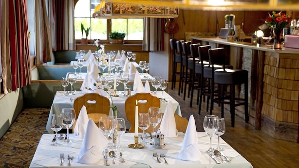 En restaurang med ett långt bord dukat för en måltid, stolar runt bordet och en bardisk i bakgrunden.