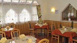 A dining area with multiple tables set for meals, wooden chairs, and a large window with floral curtains. - Zum Stadttor (Schladming)
