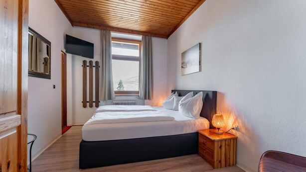 Une chambre à coucher avec un lit, une lampe de chevet, une table de chevet en bois et une fenêtre avec des rideaux.