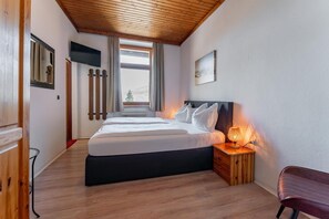 A bedroom with a bed, bedside lamp, wooden nightstand, and a window with curtains. - Gasthof Post (BRUCK AN DER GLOCKNERSTRASSE)