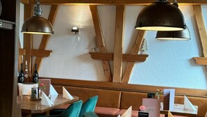 Un restaurant chaleureux avec des poutres en bois, des chaises de couleur turquoise et des luminaires suspendus.