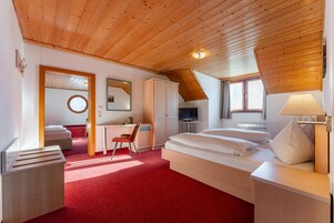 Una habitación con techo de madera, una cama, un escritorio, una silla, un televisor y una ventana.