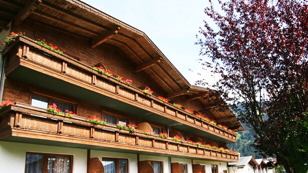 A multi-story hotel with balconies adorned with flowers, a grassy lawn, and blue lounge chairs. - first mountain Hotel Zillertal (Aschau Im Zillertal)