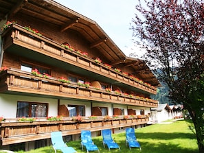 Un hotel de varios pisos con balcones decorados con flores, un césped y sillas de descanso azules.