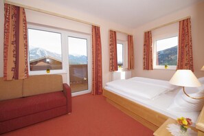 A hotel room with a bed, a red sofa, a window with a mountain view, and a lamp on the bedside table. - Hotel Restaurant Pariente (Schladming)