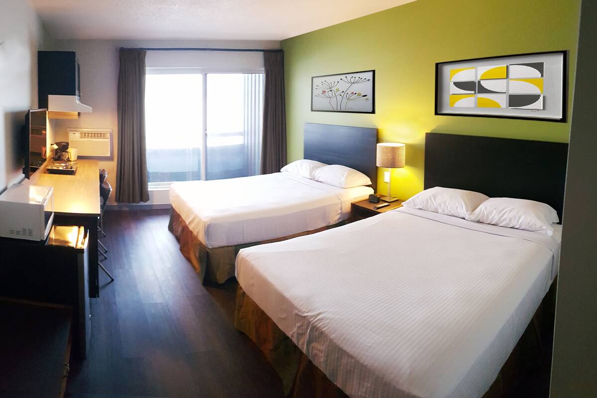 Una habitación de hotel con dos camas, un escritorio, una lámpara y obras de arte en las paredes.