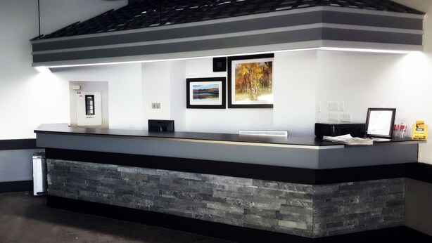 A reception desk with a stone base, framed artwork on the wall, and a small trash can to the left. - Home Away Inn (Drayton Valley)
