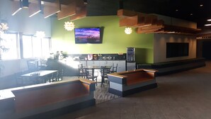 A modern restaurant interior with a green accent wall, a flat-screen TV displaying a sunset, and a seating area with wooden tables and benches. - Home Away Inn (Drayton Valley)