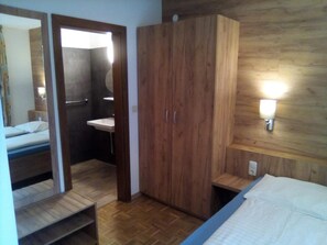 A bedroom with a wooden wardrobe, a bedside table, a bed, and a wall-mounted light fixture.