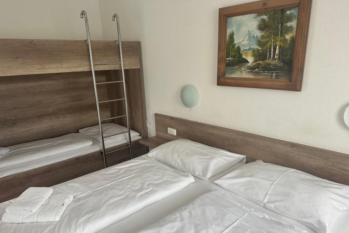 Une chambre d’hôtel avec deux lits, un lit superposé en bois, un tableau au mur et une horloge ronde fixée au mur.