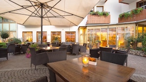 An outdoor seating area with wicker furniture and a wooden table, under a large umbrella. - Hotel Engel (Sluderno)