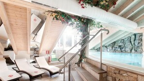 A spa area with a hot tub, lounge chairs, and a stone wall. - Hotel Engel (Sluderno)