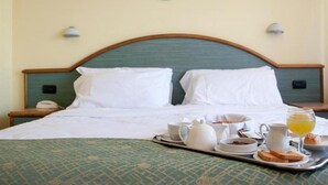 A neatly made bed with white linens, a tray with breakfast items including toast, eggs, and juice, and a wall-mounted light fixture. - Europa (Ispra)