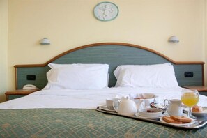 A neatly made bed with white linens, a tray with breakfast items including toast, eggs, and juice, and a wall-mounted light fixture. - Europa (Ispra)