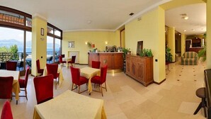 A hotel lobby with a dining area, a reception desk, and a view of the outdoors. - Europa (Ispra)