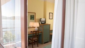 A room with a desk, chair, television, lamp, and a view of the outdoors. - Europa (Ispra)