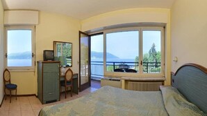 A bedroom with a bed, a desk, a chair, and a view of the sea through large windows. - Europa (Ispra)