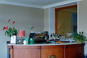 Una zona de bar con una máquina de café, botellas, vasos y un espejo.