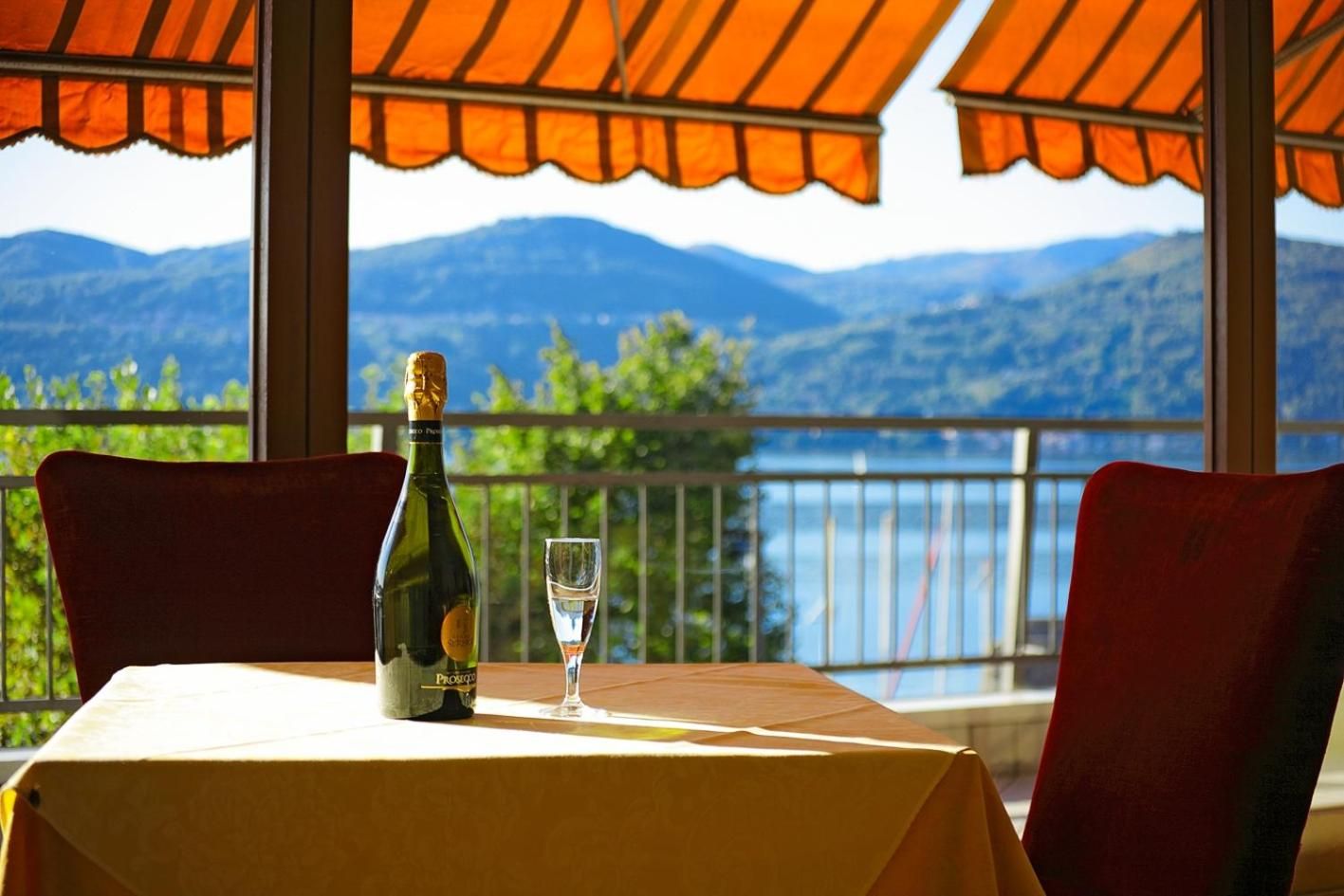 A table with a bottle and glass, red chairs, and a view of mountains and water.