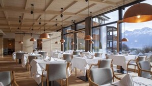 Un restaurante con vigas de madera en el techo, ventanas amplias y mesas dispuestas para comer.