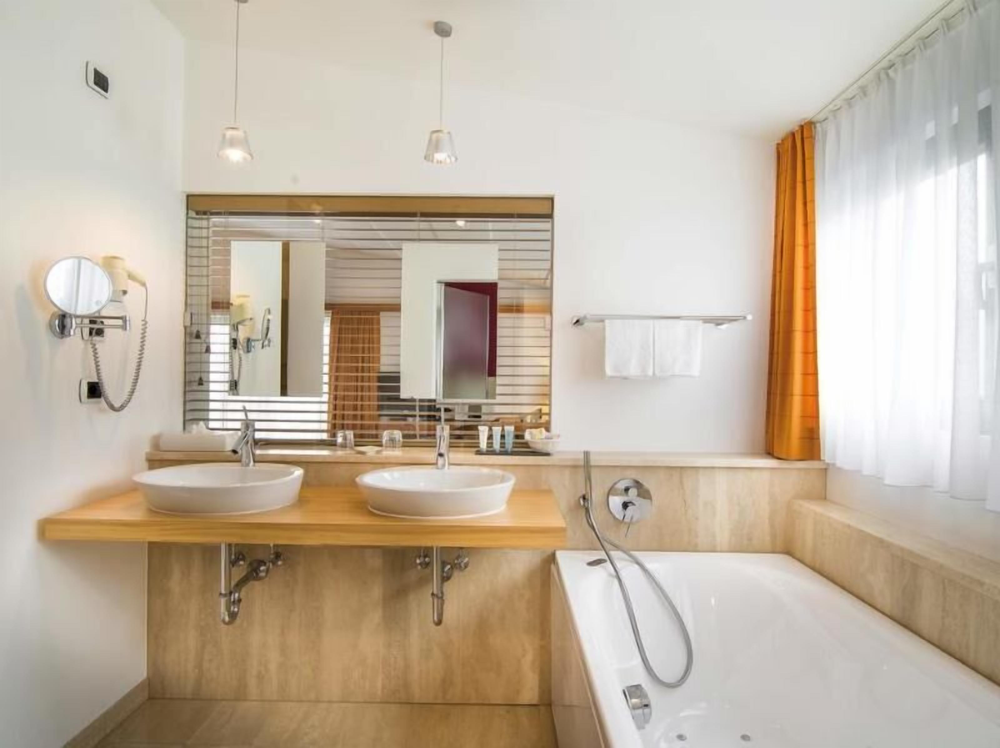 Ein modernes Badezimmer mit zwei Waschbecken, einem großen Spiegel, einer Badewanne und einem Handtuchhalter.