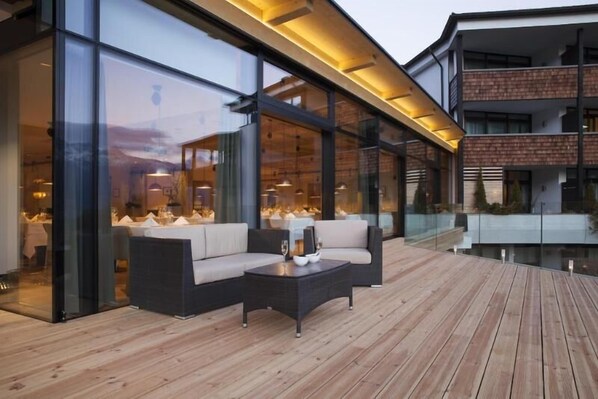 Un espace extérieur moderne, aménagé avec une terrasse en bois, des murs en verre et un coin repas visible à travers les fenêtres.
