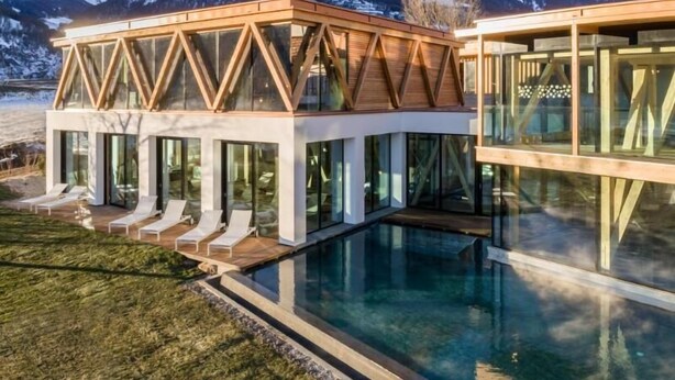 Un edificio moderno con fachada de vidrio, piscina y vistas a montañas nevadas.