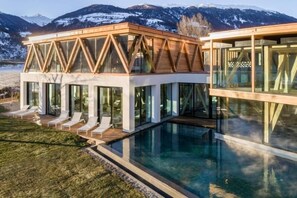 Un bâtiment moderne avec une façade en verre, une piscine et une vue sur des montagnes enneigées.