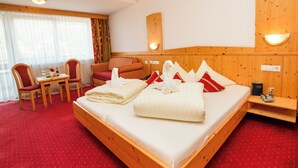 A hotel room with a large bed, a wooden headboard, a small table with chairs, and a window with curtains. - Hotel Alpina Resort (Wenns)