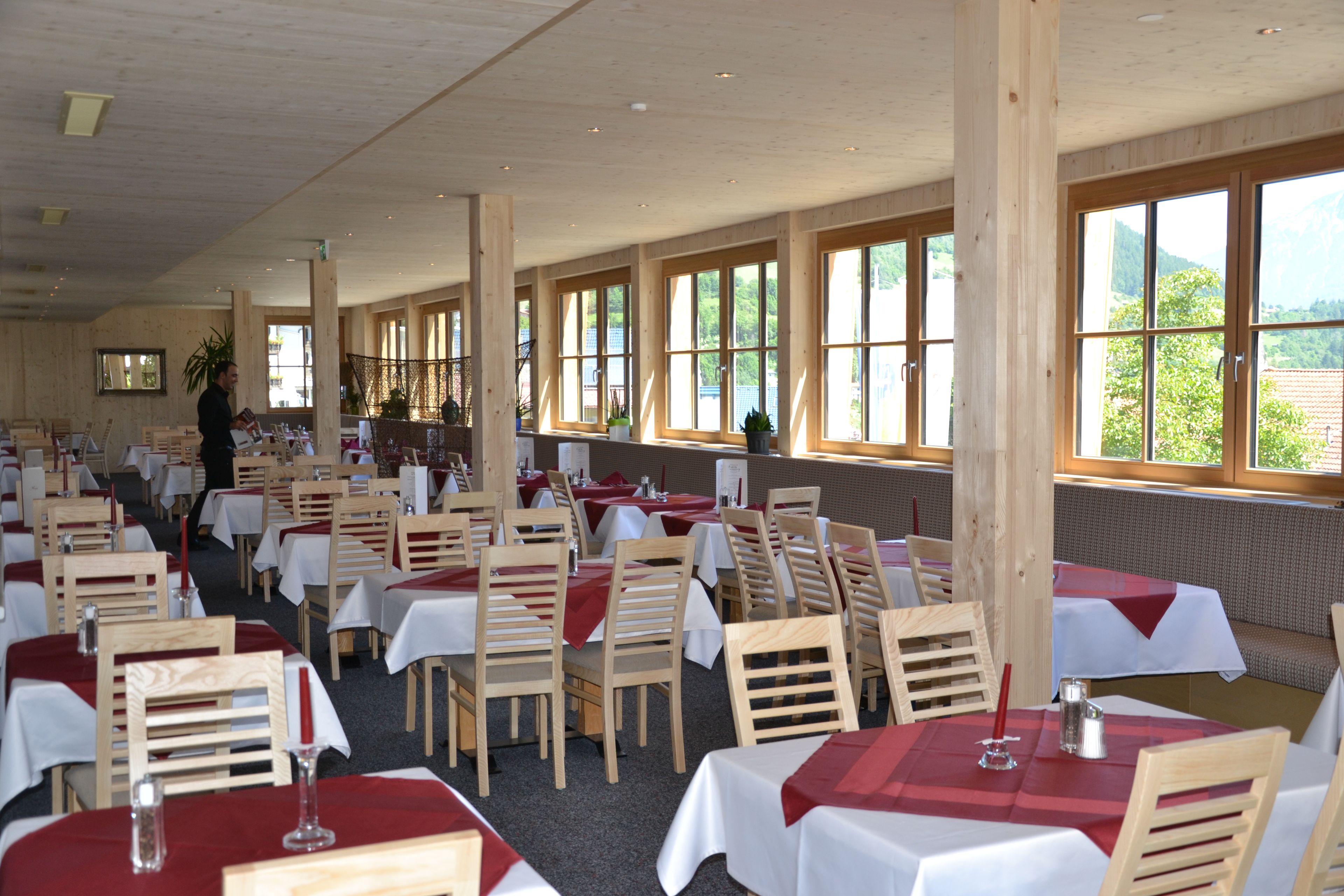 A restaurant with multiple tables and chairs, large windows, and a view of the outdoors.