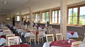 A restaurant with multiple tables and chairs, large windows, and a view of the outdoors.