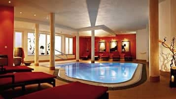 A pool area with red lounge chairs, a glass-enclosed pool, and a view of the outdoors.