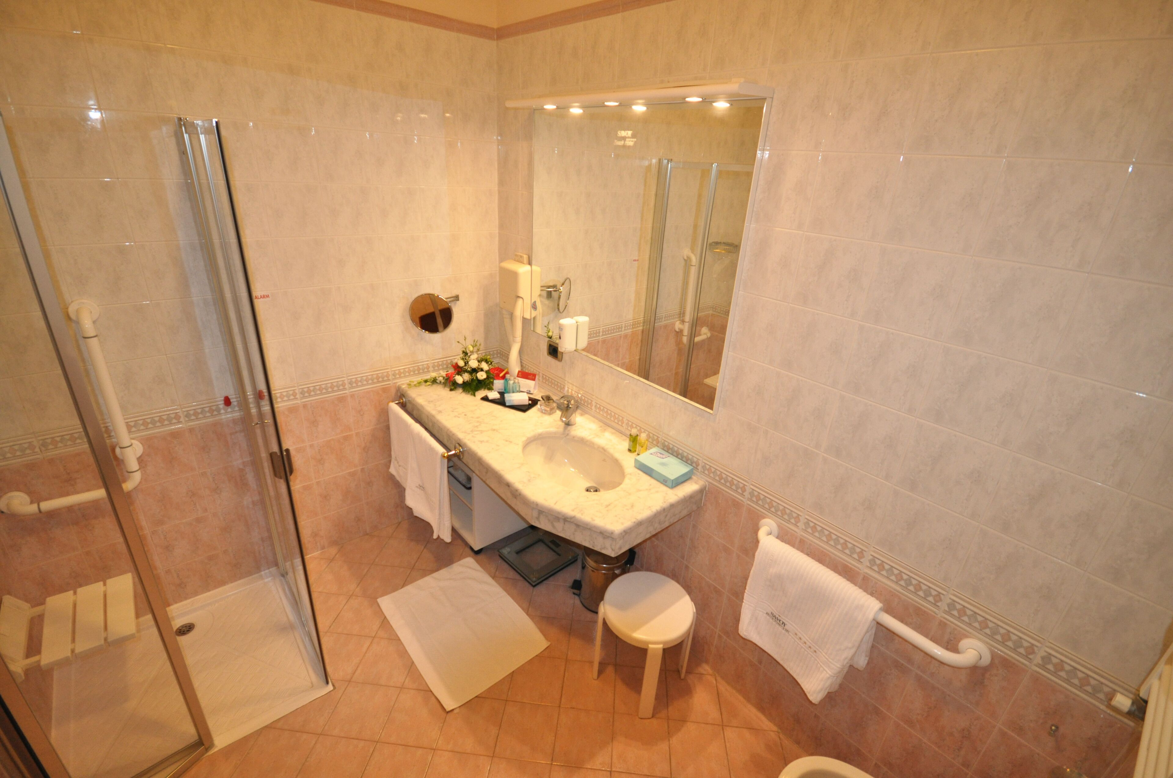 A modern bathroom with a glass-enclosed shower, a sink with a mirror above it, and a small stool.