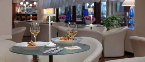 A dining area with a glass table, white chairs, and a bowl of pasta with two wine glasses.