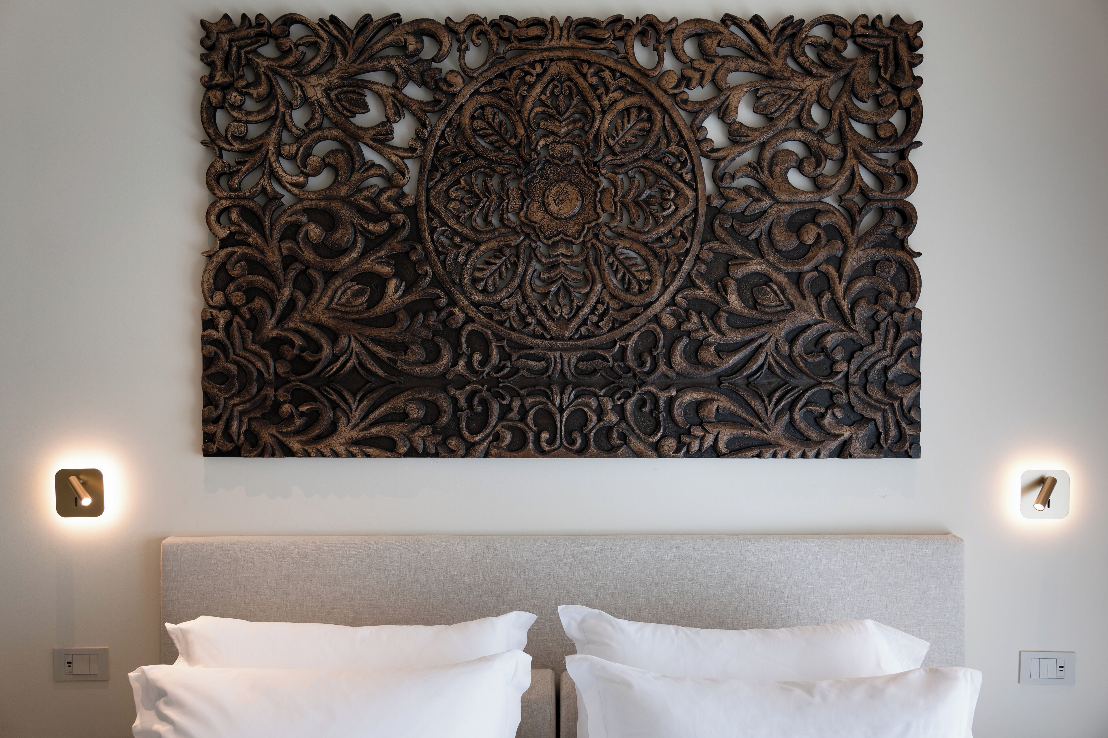 A bedroom with a decorative wall panel, two bedside lamps, and a bed with white linens.