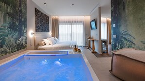 Habitación de hotel con una cama grande, un rincón de descanso, una piscina y un mural con temática tropical.