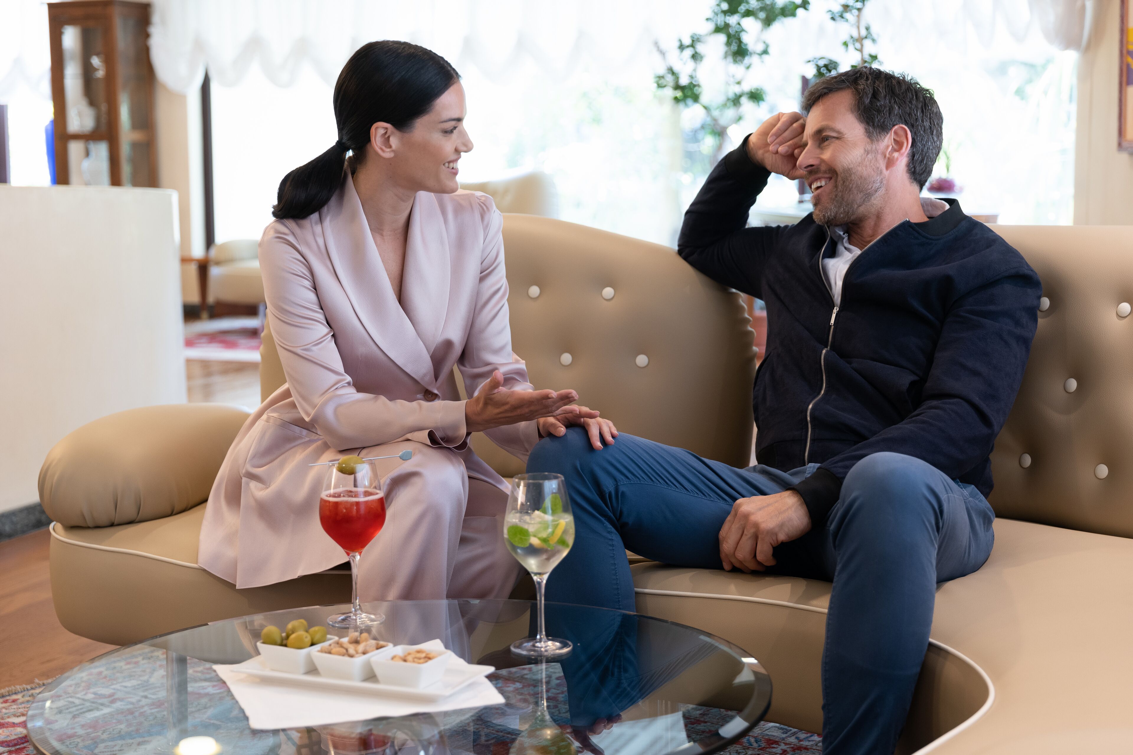 A couple sitting on a beige sofa in a well-lit room with a glass coffee table in front of them.