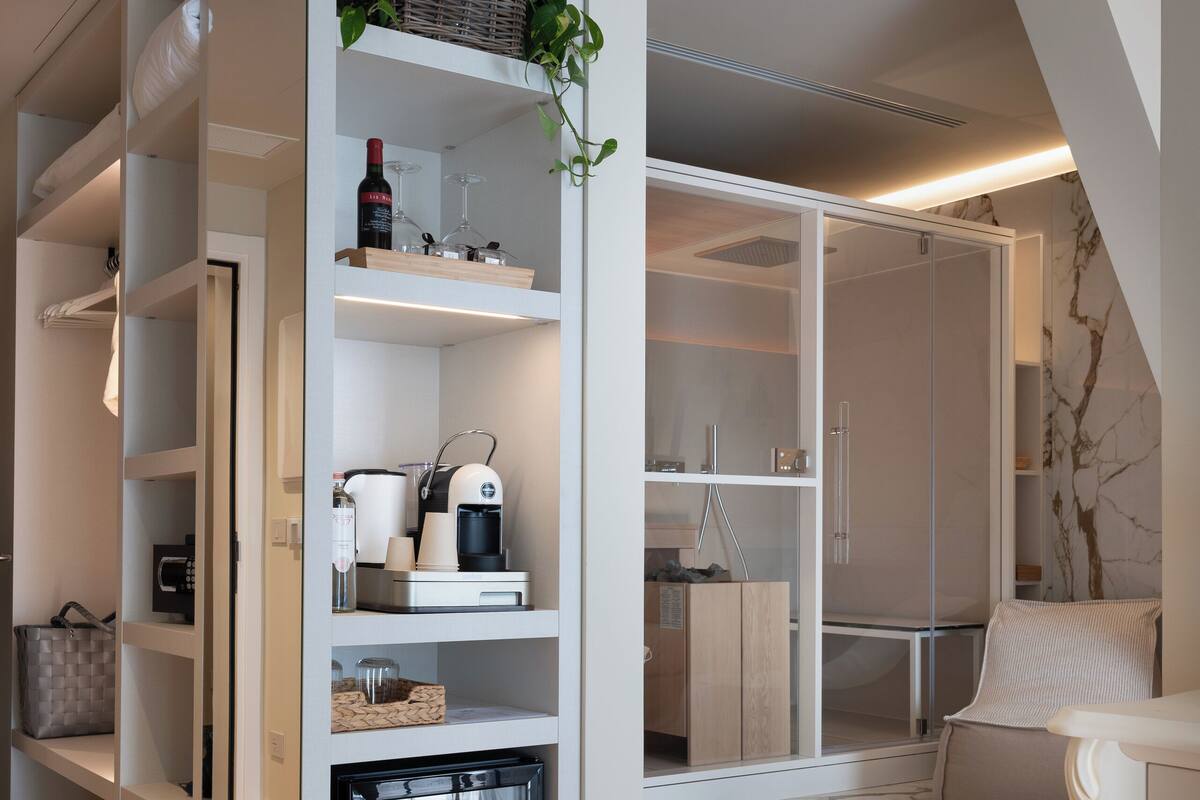 A modern interior with a built-in refrigerator, shelves with various items, a seating area with a marble floor, and a staircase leading to an upper level.