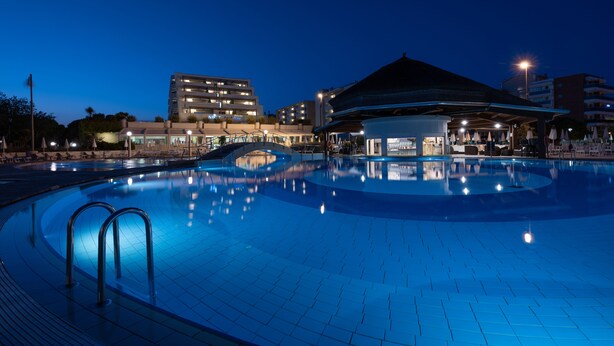 Una piscina con un entorno arquitectónico moderno, que incluye una zona cubierta y edificios adyacentes.