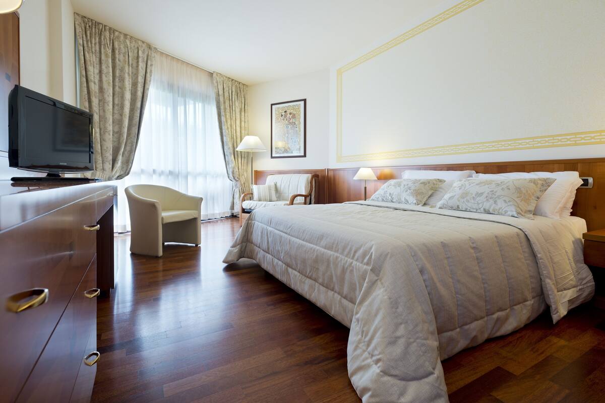 A hotel room with a bed, a desk, a television, a chair, and a lamp.