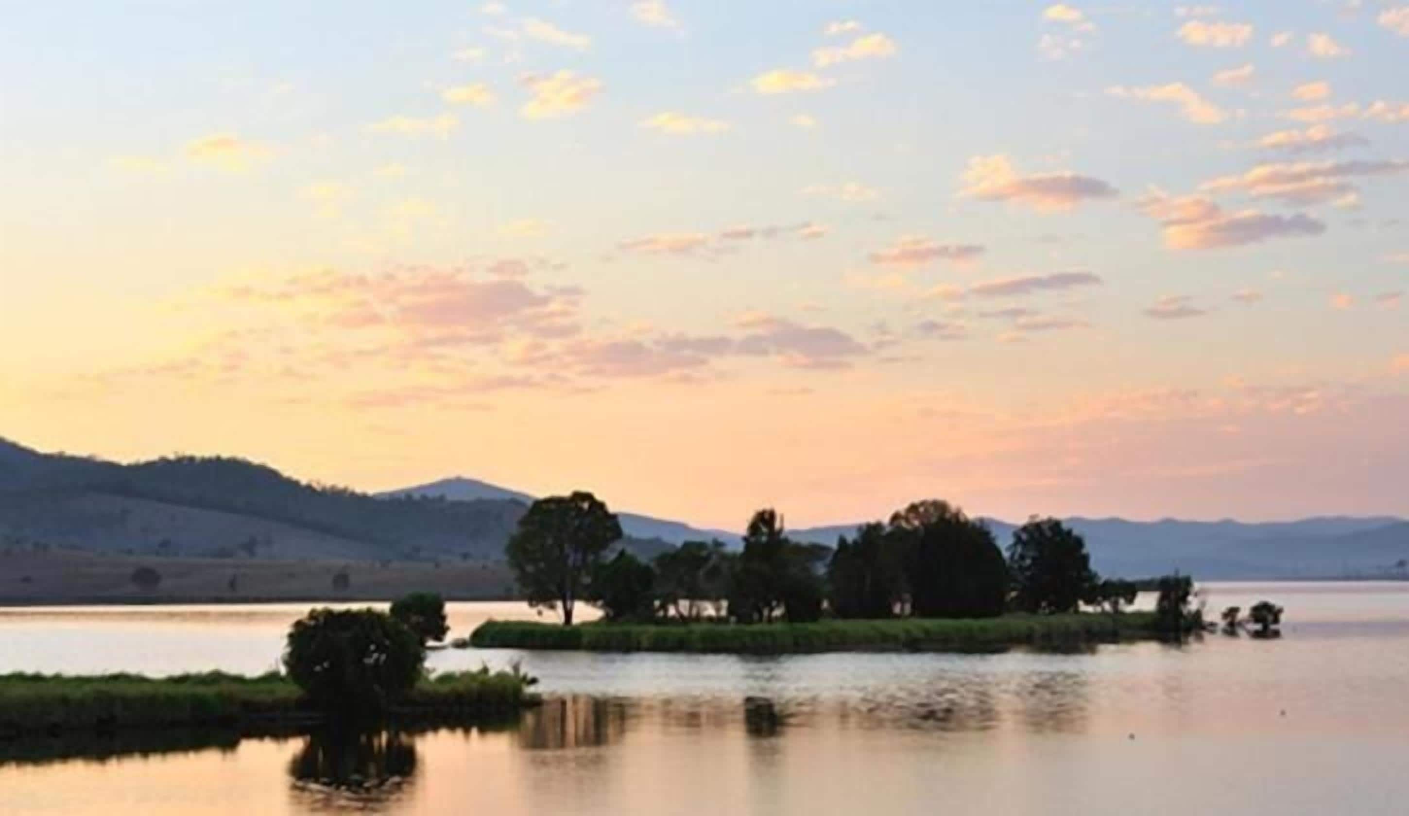 Un lago tranquilo con una pequeña isla de árboles y una cadena montañosa distante.