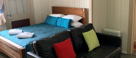 Quarto com cama de madeira, sofá de couro preto, colcha azul e branca e um espelho na parede.
