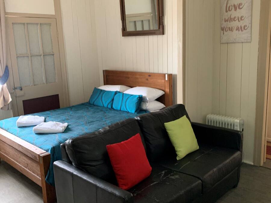 A bedroom with a wooden bed, a black leather sofa, a blue and white bedspread, and a mirror on the wall.