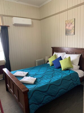 A bedroom with a wooden bed, a blue patterned bedspread, and a radiator. - Exchange Hotel Toogoolawah (Toogoolawah)