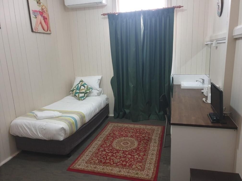 Un dormitorio pequeño y ordenado con cama, escritorio con computadora, una silla y un ventanal con cortinas.